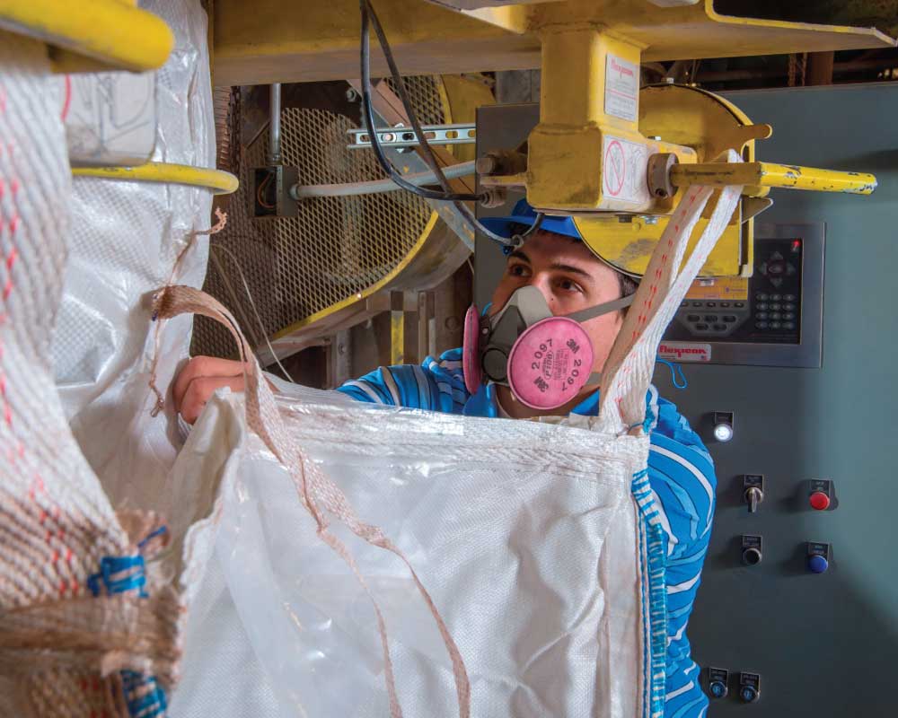 Person in respirator operating a hammer mill