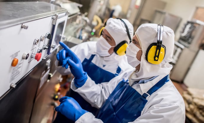 Two workers in protective clothing in a custom toll processing factory