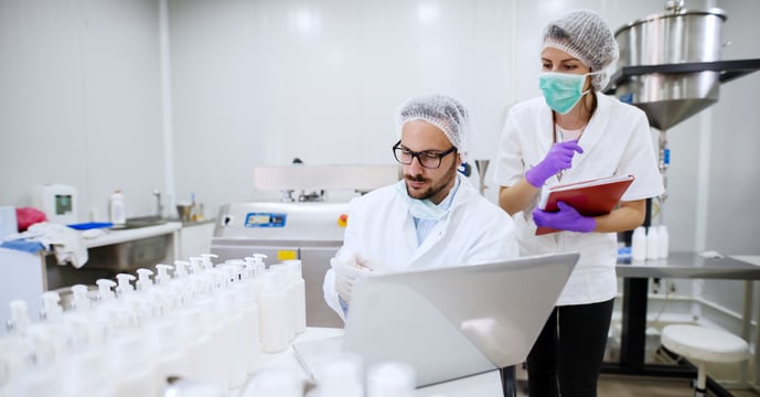 Two scientists working in a lab wearing protective clothing.